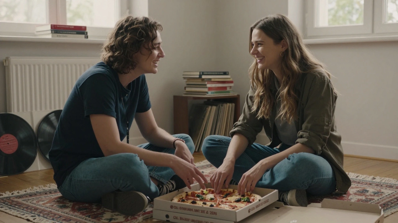 Two people share pizza and conversation on a rug surrounded by books and records in a cozy apartment.